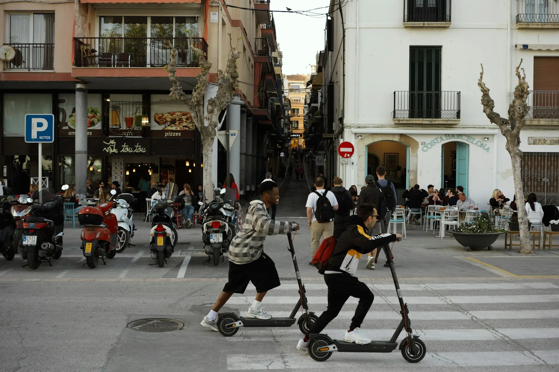 Dos personas cruzan una calle en patinete en un municipio